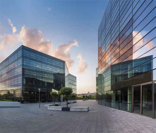 A set of modern office buildings reflecting the sky during sunset.
